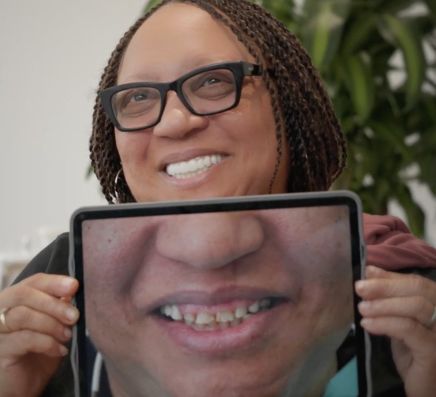 Dorothy smiling, holding up a tablet that shows her smile before treatment.